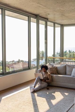 African american woman working on laptop in sunlit coastal living room with ocean view