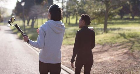 Friends walking in sunlit park holding gimbal and coffee during golden hour
