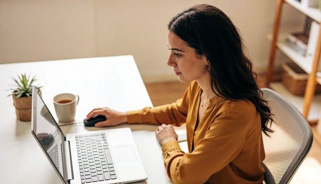Woman working on laptop at minimalist home office desk, typing, focused remote work