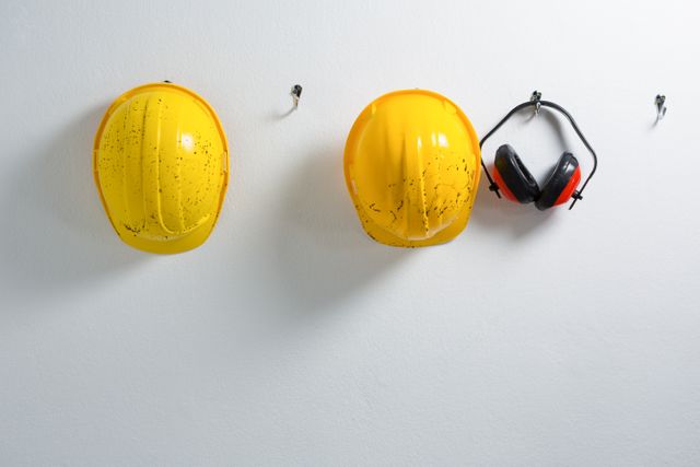 Hard hats and earmuffs hanging on hook against wall