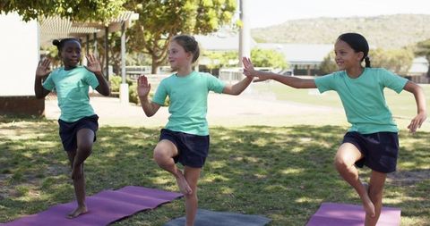 Multicultural teenage girls practicing yoga balance on school campus lawn during outdoor pe