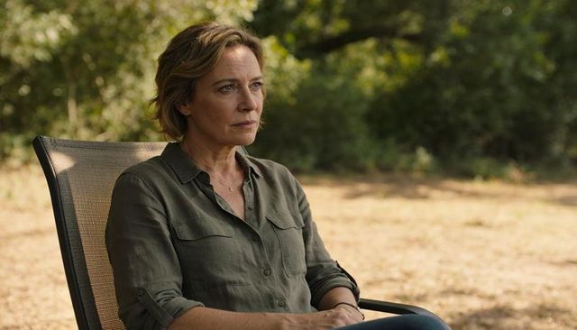 Contemplative middle-aged woman sitting in garden chair on sunny afternoon wearing olive-green shirt