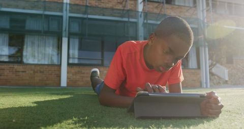 Young Boy Engaged in Tablet Gaming Outdoors Near School Building