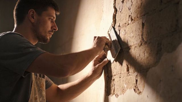 Repairing and smoothing cracked interior plaster wall with trowel, focused tradesman