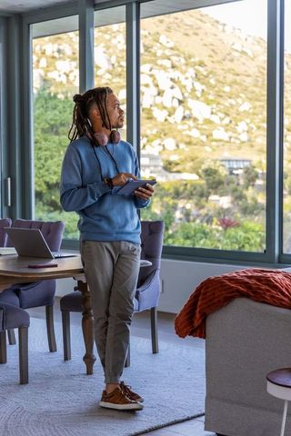 African american man standing with tablet by window for remote work in modern home