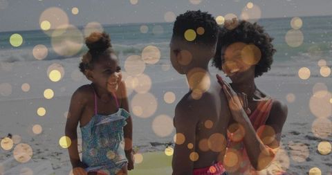 Laughing family playing on sunny beach with children splashing and hugging, soft bokeh lights