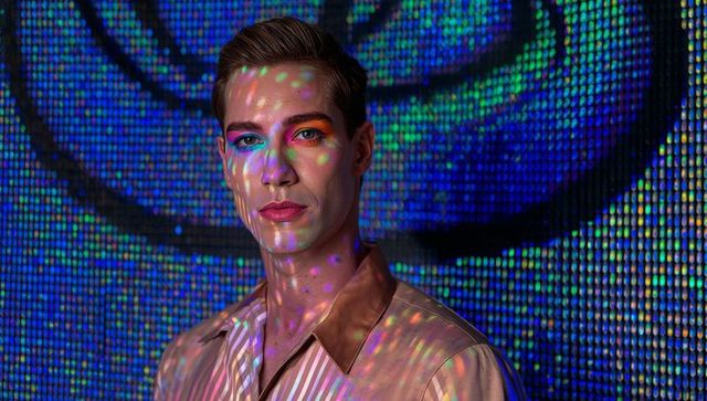 Posing male model with led projections and neon makeup on pixelated blue backdrop