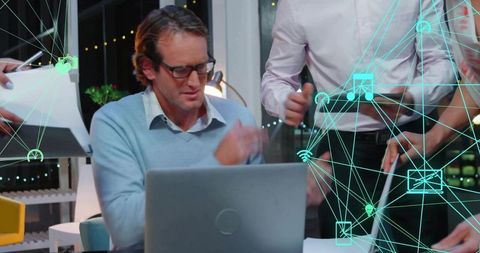 Team working late around laptop with turquoise network icons overlay, urban workspace