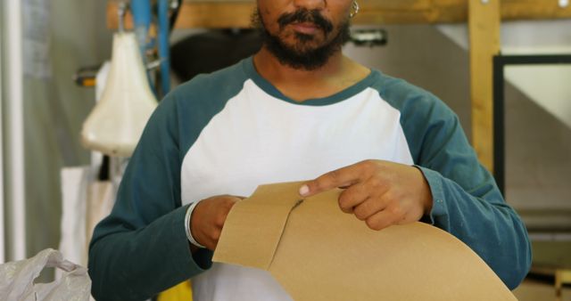 Picture of African American man working on cardboard piece in workshop. Suitable for use in DIY crafting, handwork projects, and construction tutorials publications.