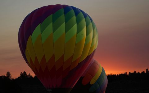 Colorful Hot Air Balloons Inflating at Sunrise Over Forested Horizon with Warm Sky