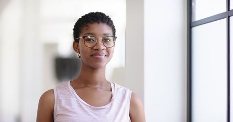 Smiling professional woman wearing glasses standing in bright modern office hallway