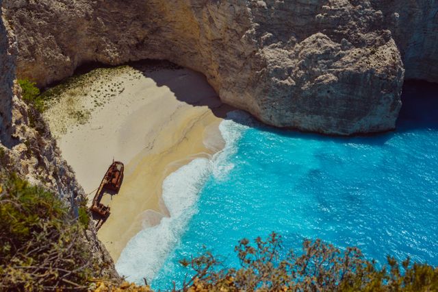 Idyllic view of a shipwreck resting on a secluded beach framed by tall cliffs and crystal clear turquoise water. Perfect for travel advertisements, tourism brochures, adventure promotions, and landscape art. The beautiful scenery creates a sense of curiosity and longing for exploration.