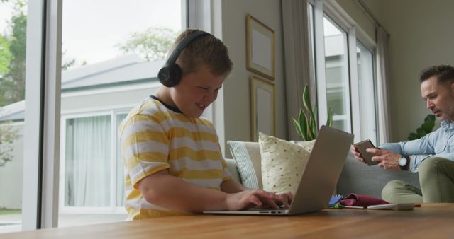 Young Boy with Down Syndrome Using Laptop with Headphones, Parent in Background - Download Free Stock Images Pikwizard.com