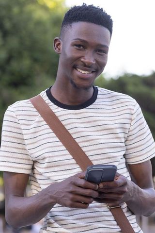 African american man smiling and texting on smartphone in park casual daylight portrait