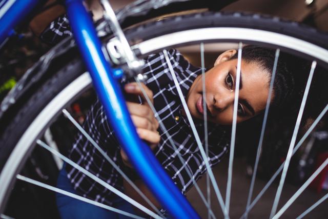 Close-up view of a female mechanic repairing a blue bicycle in a workshop. Ideal for promoting services related to bicycle maintenance, mechanics, and repair shops. Great for illustrating concepts of skilled labor, professional services, and mechanical work.