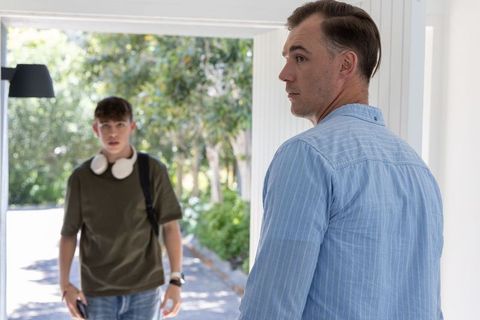 Father looking back watching teen entering driveway with backpack and headphones