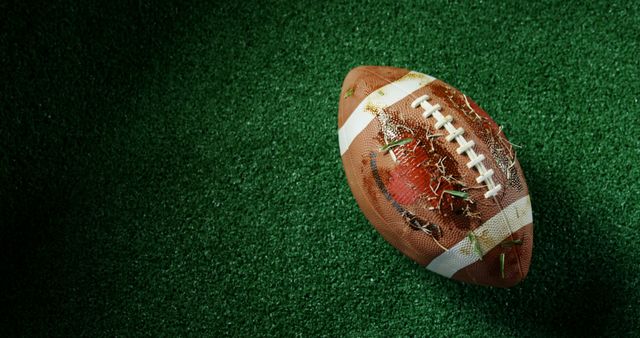 Close-up of a worn football lying on a turfed field. Great for sports articles, American football promotions, game day materials or equipment marketing.