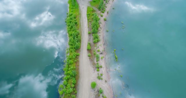 A narrow dirt path divides a lush green landscape and a tranquil blue body of water, with copy space. The aerial perspective emphasizes the serene and untouched beauty of this natural environment.