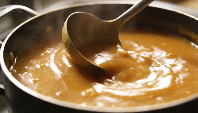 Rich brown gravy simmering in pot with long-handled ladle stirring glossy savory sauce