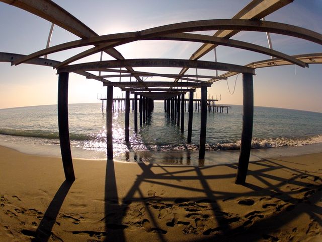 Sunlit beach pier taken from a low angle under the structure with ocean view in the background. Great for beach vacation promotions, travel postcards, coastal living magazines, and relaxation-themed websites.