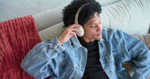 Relaxing african american man listening to music on headphones while reclining on couch