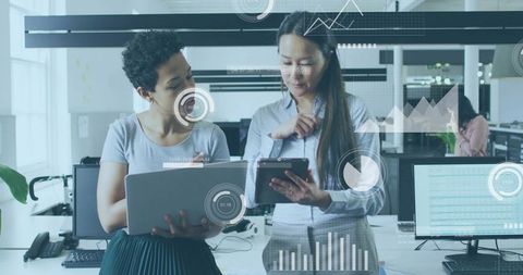 Businesswomen Collaborating with Tablet and Laptop in Modern Office Showing Data Overlays