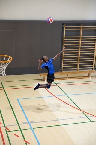 African american teen jumping and spiking volleyball indoors on gym court with hoop