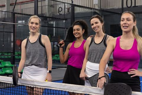 Diverse women playing padel together on indoor court, teamwork in vibrant sportswear