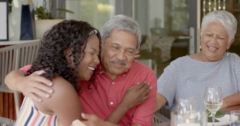 Multigenerational family hugging and laughing around sunroom table with wine glasses