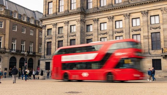 Red double-decker bus blurring across historic neoclassical plaza with pedestrians