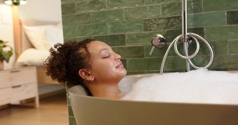 African american woman relaxing in freestanding bubble bath with green tile backdrop view