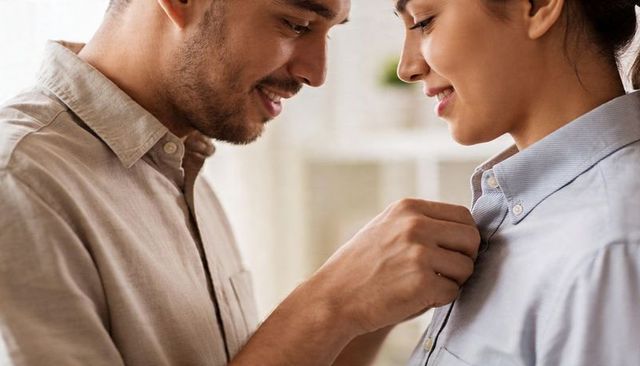 Couple fastening shirt collar button, sharing tender romantic moment at home