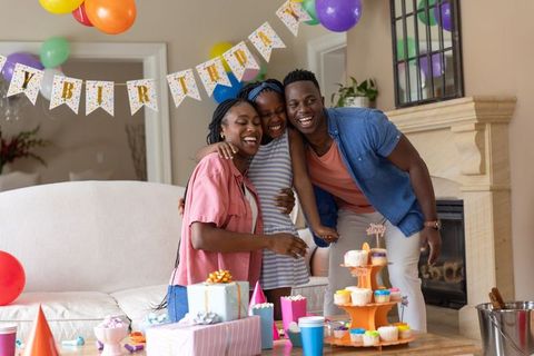 African american family hugging daughter at birthday party with cupcakes gifts balloons