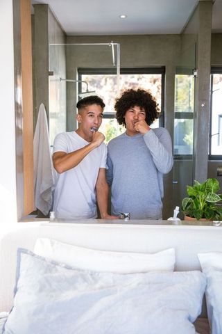 Male friends in loungewear brushing teeth in modern bathroom