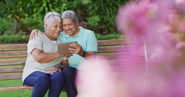 Image of happy biracial senior couple using tablet in garden. active retirement lifestyle, senior relationship and spending time with technology concept.