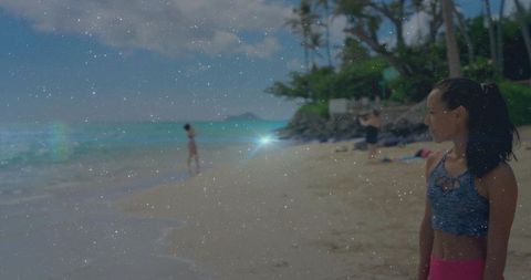 Standing athletic woman on tropical beach wearing blue top and pink bottoms with sun flare