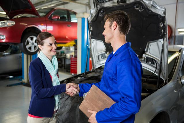 Satisfied customer shaking hands with mechanic at repair garage