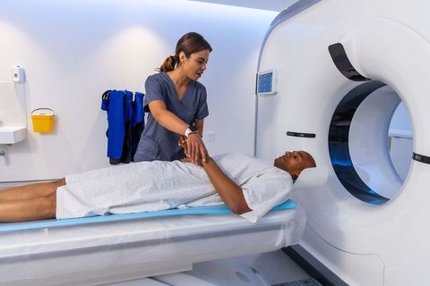 Nurse holding african american patient's hand during ct scan for calming reassurance