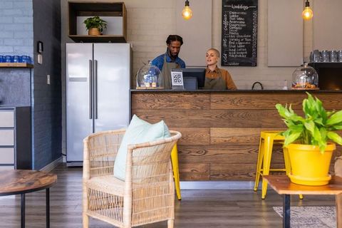 Diverse baristas serving at rustic wooden counter using pos and displaying fresh pastries