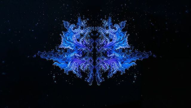 Flowing symmetrical ink splash forming mirrored butterfly with cyan and indigo tendrils