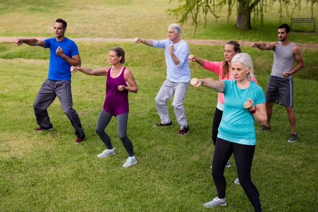 Group of diverse individuals participating in a fitness class in a park. Ideal for promoting outdoor exercise, community health programs, and active lifestyle initiatives. Suitable for use in health and wellness campaigns, fitness blogs, and advertisements for fitness classes or outdoor activities.