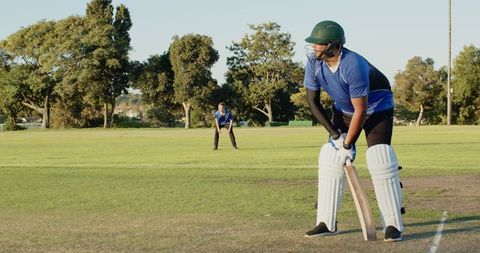 Cricket batsman at crease wearing green helmet and blue uniform preparing to face delivery