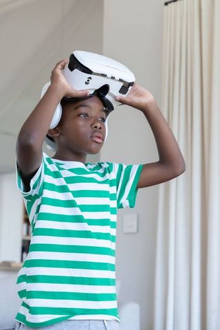 African american boy exploring virtual reality wearing white headset and headphones at home