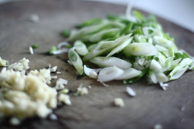 This image shows a close-up view of freshly chopped spring onions and minced garlic placed on a wooden cutting board, with a rustic appearance. Ideal for illustrating recipes, food blogs, culinary websites, and cooking tutorials. It provides a natural, organic feel perfect for content related to healthy eating, vegan recipes, and vegetarian dishes.