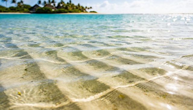 Turquoise shallow lagoon revealing rippling sand ridges and sunlit caustics on tropical shore