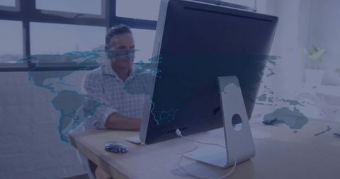 Executive working at desktop with world map overlay illustrating global connectivity