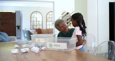 Black grandmother teaching granddaughter recycling and sorting paper and plastic at home