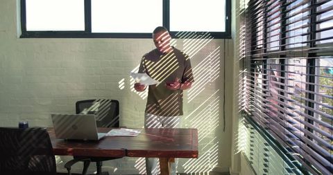 African american man checking smartphone while reviewing documents in sunlit office