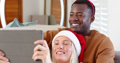 Diverse Couple Smiling at Tablet in Festive Holiday Setting