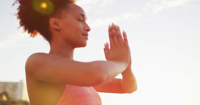 Woman practicing yoga outdoors at sunrise. Her hands are in namaste position, representing peace and mindfulness. Great for promoting mental health, fitness routines, yoga classes, wellness retreats, and outdoor activities.
